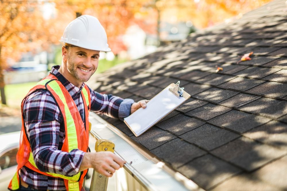 A,Man,With,Hard,Hat,Standing,On,Steps,Inspecting,House Roofing Inspections in Ottawa. A man with a hard hat is standing on the steps of a ladder. Inspecting the house roof