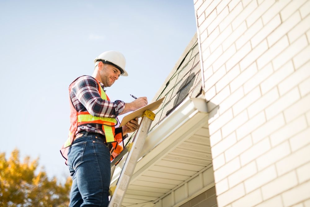 A,Man,With,Hard,Hat,Standing,On,Steps,Inspecting,House Roofing Inspections in Ottawa. A man in a hard hat stands on a ladder, inspecting the house roof.