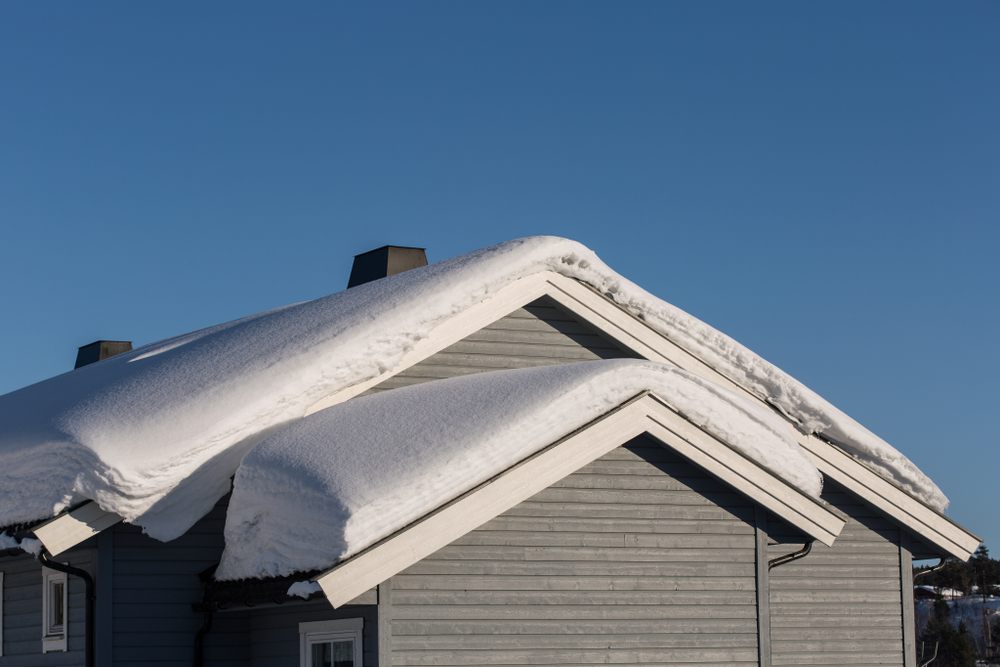 Winter Roof Repairs in Ottawa: What Homeowners Need to Know? roofs of gray wooden houses covered with thick snow layer against blue clear sky background.