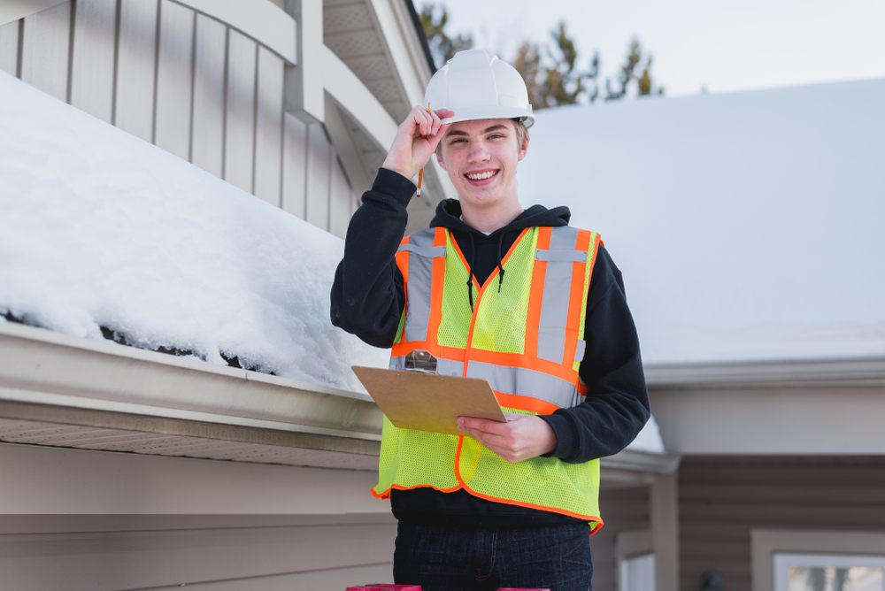 Winter Roof Inspections: What Ottawa Homeowners Should Know? Happy home inspector on a ladder while holding a clipboard during winter.