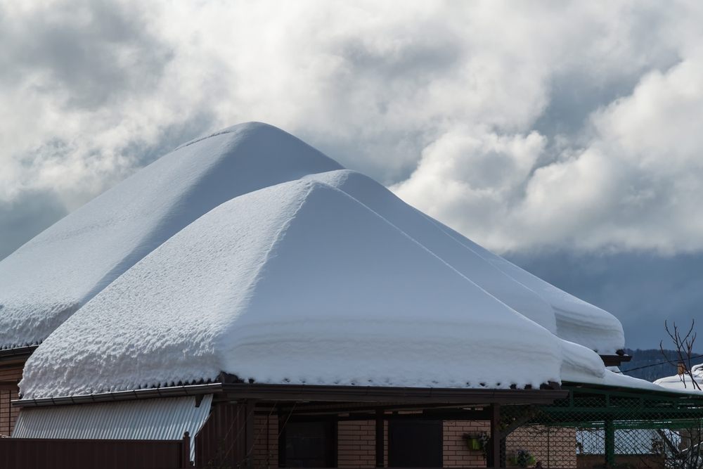 Essential Roof Maintenance Tips to Protect Your Ottawa Home This Winter? Snow drifts on the roof after the snowfall. In the background, the sky is covered with gray clouds. Roofs of the house, garage and shed in the snow. Three snow pyramids