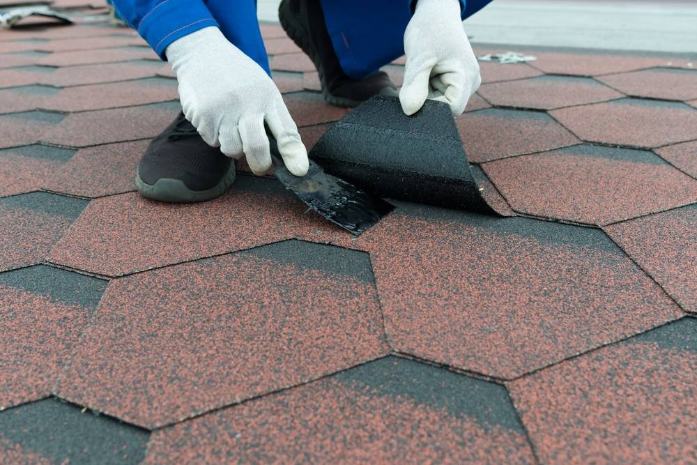 The Complete Guide to Post-Winter Roof Maintenance in Ottawa. The hands of a worker in white gloves apply black mastic with a spatula to repair the soft roof.