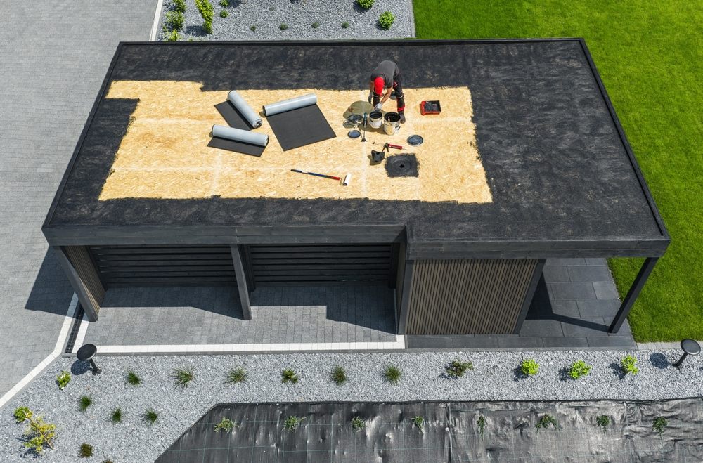 Maximizing the Lifespan of Flat & Metal Roofing in Ottawa. A team is working on the roof of a contemporary building, applying EPDM roofing materials while surrounded by a well-kept yard and clear skies.