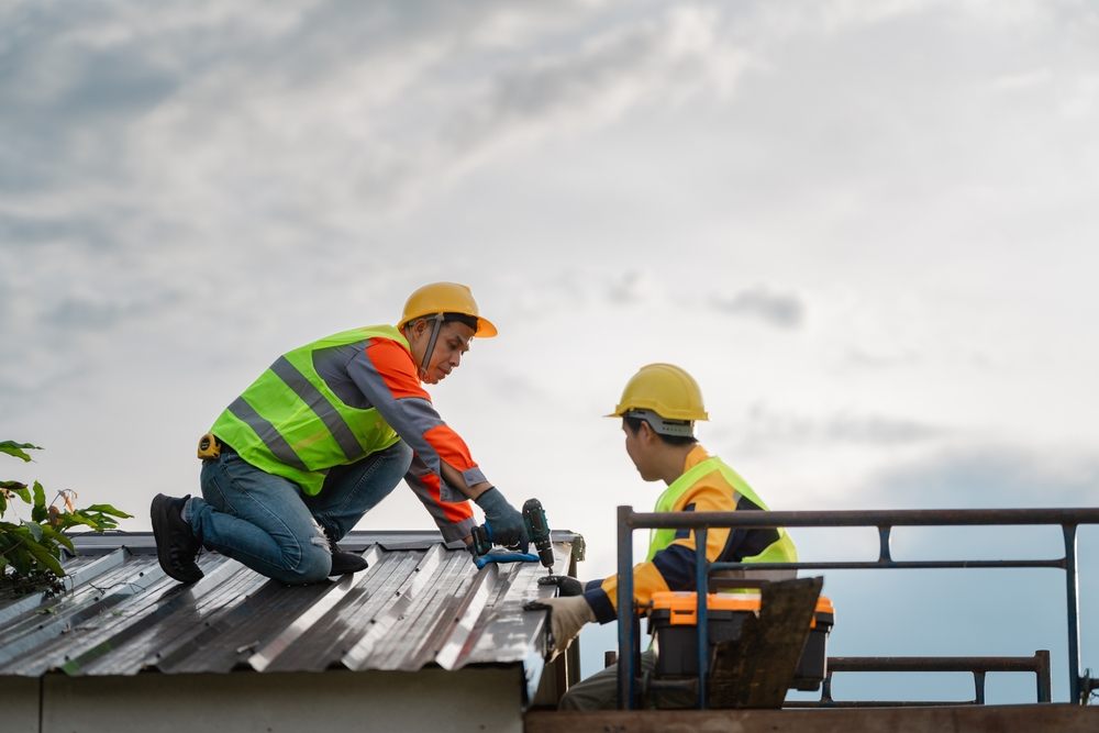 Why Choose Metal Roof Repair Services from Trusted Ottawa Roofing Companies? Two skilled construction workers collaborate on repairing a metal roof. They showcase dedication and safety while emphasizing teamwork in a construction setting.